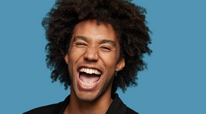 A man with coily hair smiling with closed eyes